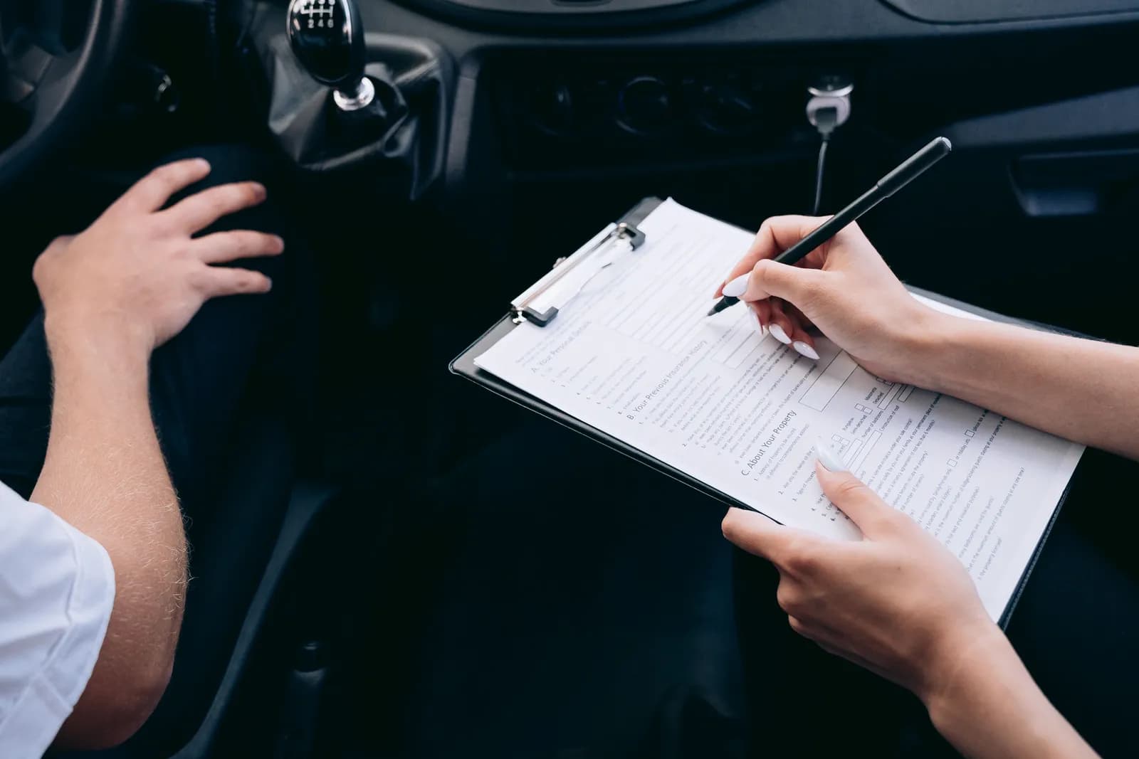 Two people filling out a form on a clipboard inside a car