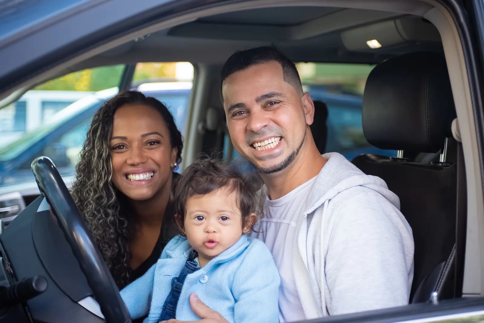 A smiling family with a baby sitting in a car