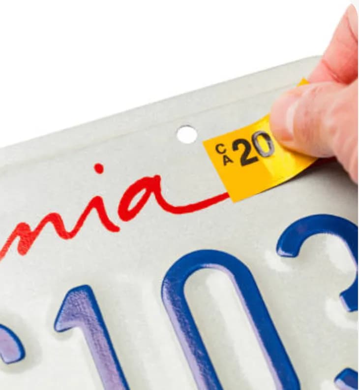 A hand placing a registration sticker on a license plate
